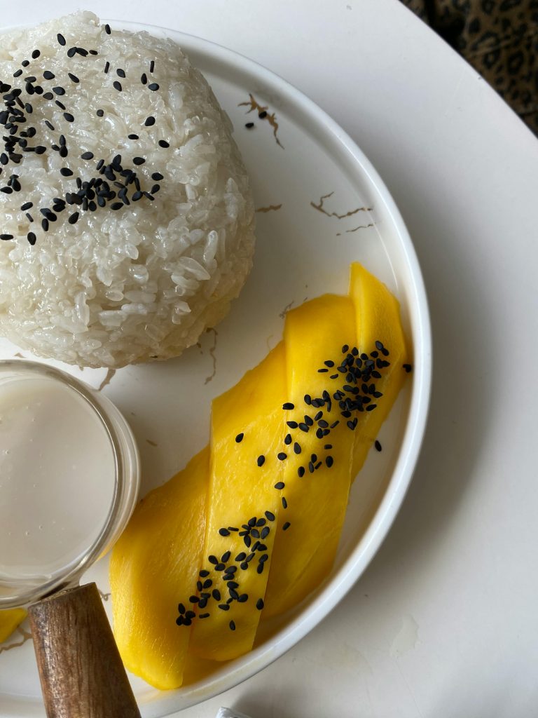 A close-up of mango sticky rice with black sesame seeds on a white plate, showcasing vibrant colors.