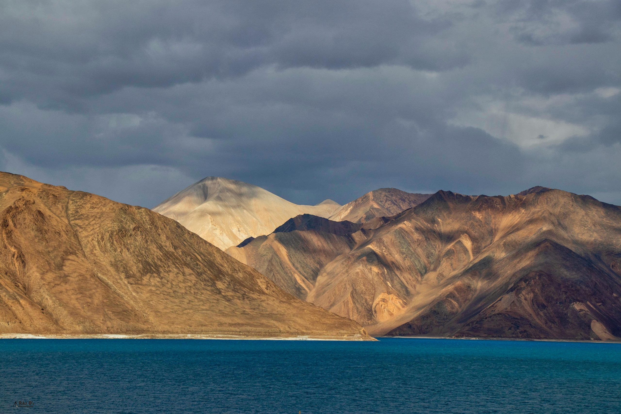 Stunning landscape of Pangong Lake with the majestic Himalayan mountains under a dramatic sky.