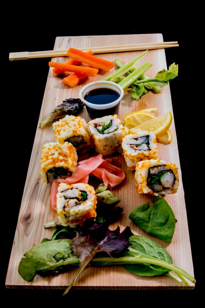 Vibrant sushi platter with fresh vegetables and soy sauce on a wooden board.